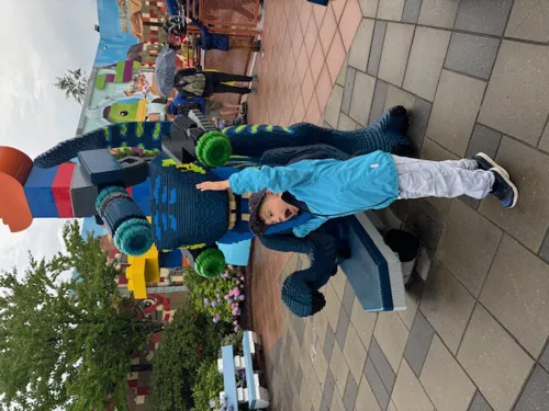 Boy underneath LEGO® sculpture with arms in the air. 